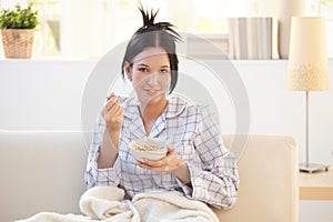 Girl in pyjama having cereal breakfast on couch