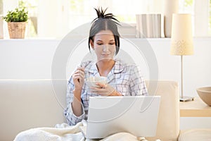 Girl in pyjama having cereal using laptop