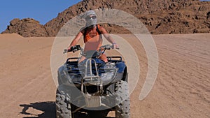 Girl on a quad bike rides through the desert of egypt on background of mountains