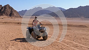 Girl on a Quad Bike Rides through the Desert of Egypt on Background of Mountains