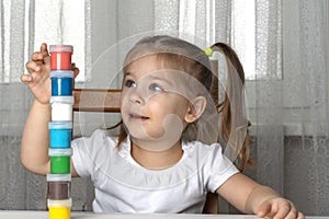 a girl in quarantine sits and builds a tower of cans of colored paints