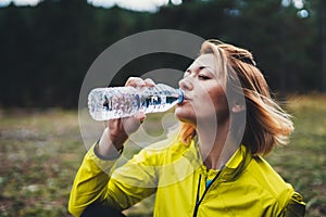 Girl quenches thirst after fitness. Smile person drinking water from plastic bottles relax after exercising sport outdoors, woman