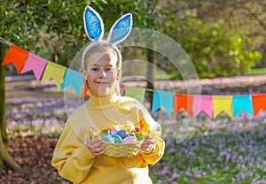 girl with rabbit ears on her head and a basket with Easter eggs in the park