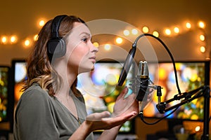 A girl radio host in a cozy atmosphere broadcasts with a studio microphone. Stream, live broadcast, blogging. Pastes