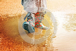 Girl in rain boots is standing in a puddle