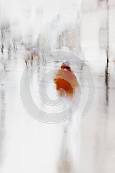 Girl in rain walking with umbrella in city. Unrecognizable person in motion blur