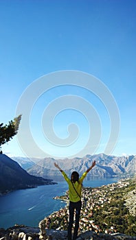 Girl with raised arms happy journey. Admiring the Boka Bay in Montenegro. Vertical view