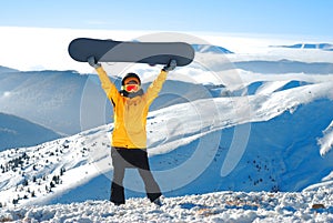 Girl raises snowboard up against panoramic winter mountain