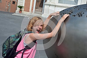 Girl reaches funnily loud in a piece of art in the city of Pisa, Italy