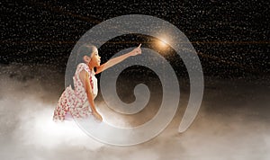 A girl reaching for the star, sitting on a cloud in dark sky, night time. Concepts of fulfilling your dream, wish, goal, and doing