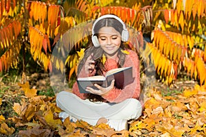 Girl read book on autumn day. Little child enjoy learning in autumn park. Kid study with book. Autumn literature concept