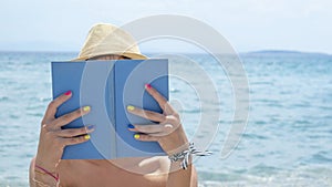 Girl reading a book on the beach wearing straw hat