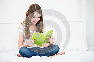 Girl reading book on bed at home