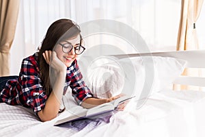 Girl reading a book in bed, lying on her stomach smiling happy