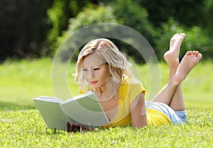 Girl reading the book. Blonde beautiful young woman with book lying on the grass. Outdoor. Sunny day