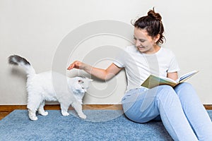 Girl reading book at cozy home. Girl smiling and petting furry cat