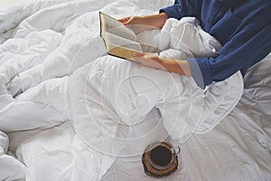 Girl reading book and drinking coffee on the bed