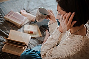 Girl reading a book and drinking coffee in bed feet on the wall.