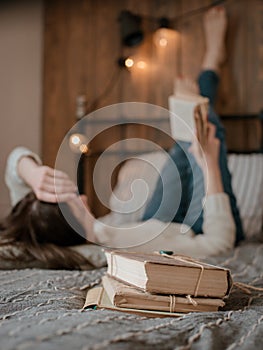 Girl reading a book and drinking coffee in bed feet on the wall.