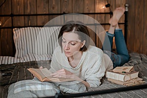 Girl reading a book and drinking coffee in bed feet on the wall.