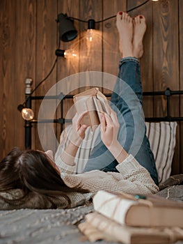 Girl reading a book and drinking coffee in bed feet on the wall.