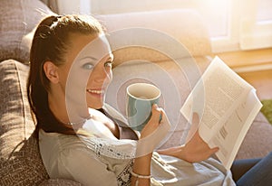 Girl reading book and drinking coffee on sofa