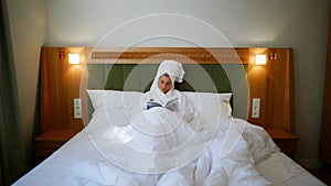 a girl reading a book. Girl after showering read a book in bed in her bathrobe. Hotel room. Bright cozy room. White bed