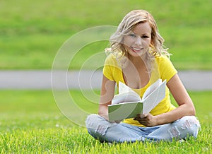 Girl reading the book. Happy blonde beautiful young woman with book sitting on the grass. Outdoor