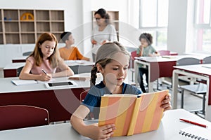 girl reading book near multiethnic classmates