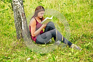 The girl is reading a book in the park in the summer
