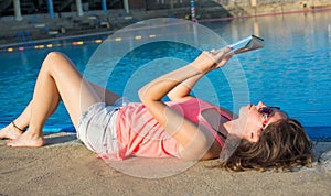 Girl reading a book by the pool.