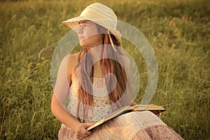 Girl reading the book on rural landscape at meadow