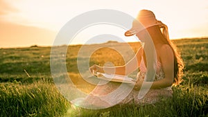 Girl reading the book on rural landscape at sunset