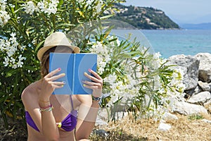 Girl reading a book in shade near the beach with rocks in background