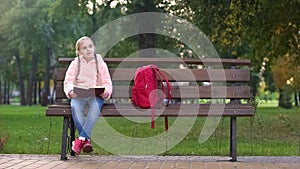 Girl reading book, sitting on bench in park, doing homework outdoors, study