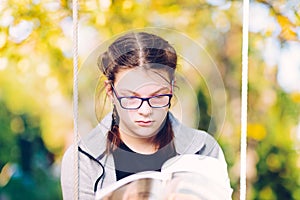 Girl reading a book while sitting on a garden swing - focused gi