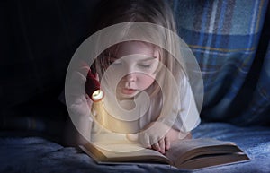 Child reading a book under the covers. Immersion into the magical world