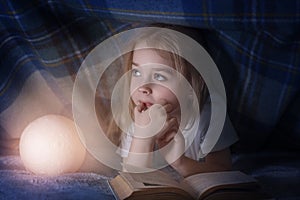 Child reading a book under the covers. Immersion into the magical world