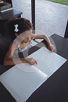 Girl reading braille at desk in library