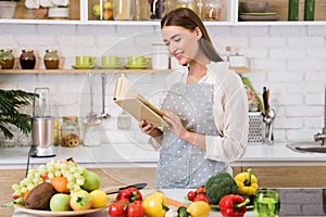 Girl reading cookbook in the kitchen, looking for recipe