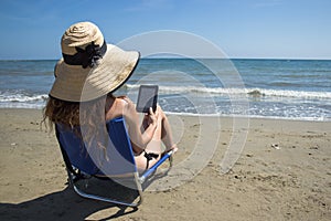 A girl reading ebook on a chair on the beach