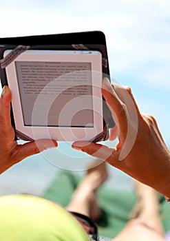 Girl reading an ebook lying on sun loungers on the beach