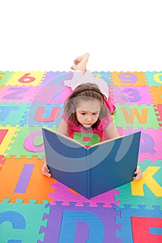 Girl reading kids book lying on alphabet floor mat