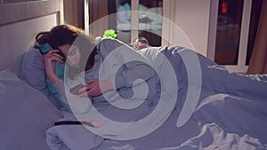 A girl reading a message on her cell phone at night lying in bed