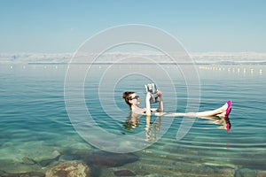 Girl reading newspaper floating on surface Dead Sea enjoy summer sun and vacation. Recreation tourism, healthy lifestyle, free tim