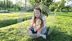 Girl reading outdoors to her little teddy bear.  girl with toys plays on the green lawn