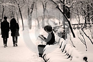 Girl reading in the snow, sitting on a bench