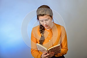 A girl reads the Bible while sitting on a chair on a blue background. The inscription in Russian -