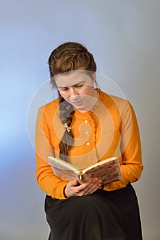 A girl reads the Bible while sitting on a chair on a blue background. The inscription in Russian -