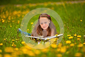 A girl reads a book in the meadow.